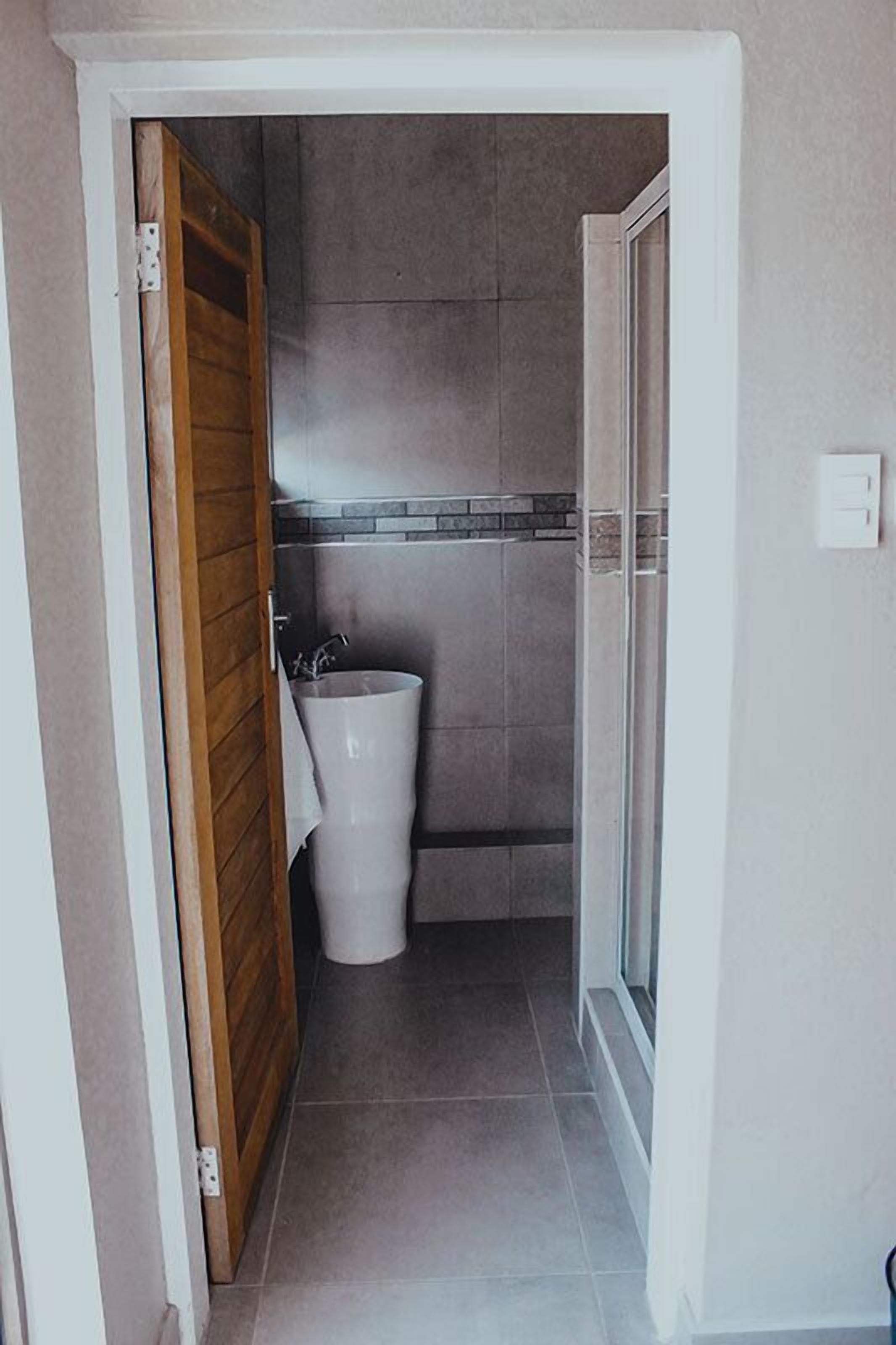 A narrow hallway leading to a bathroom with tiled walls, a shower, and a trash bin.