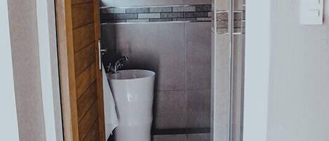 A narrow hallway leading to a bathroom with tiled walls, a shower, and a trash bin.