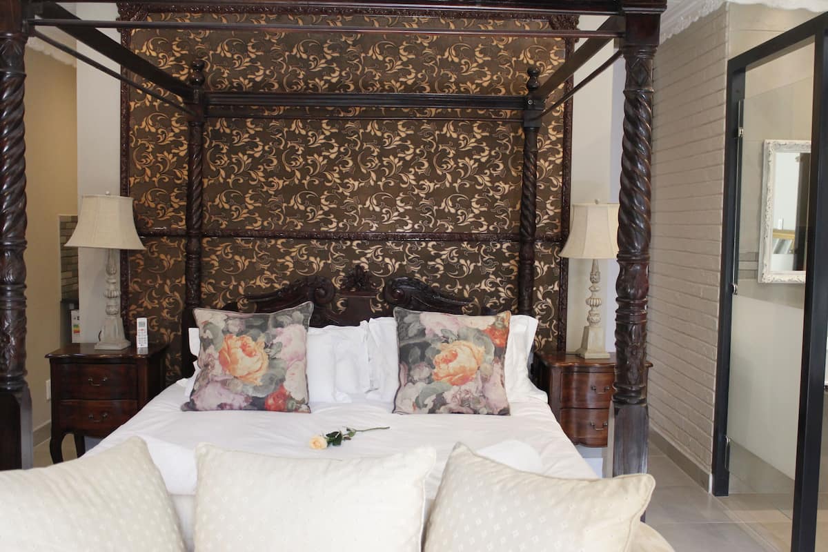 A four-poster bed with floral pillows, a bedside table with a lamp, and a mirror on the wall.