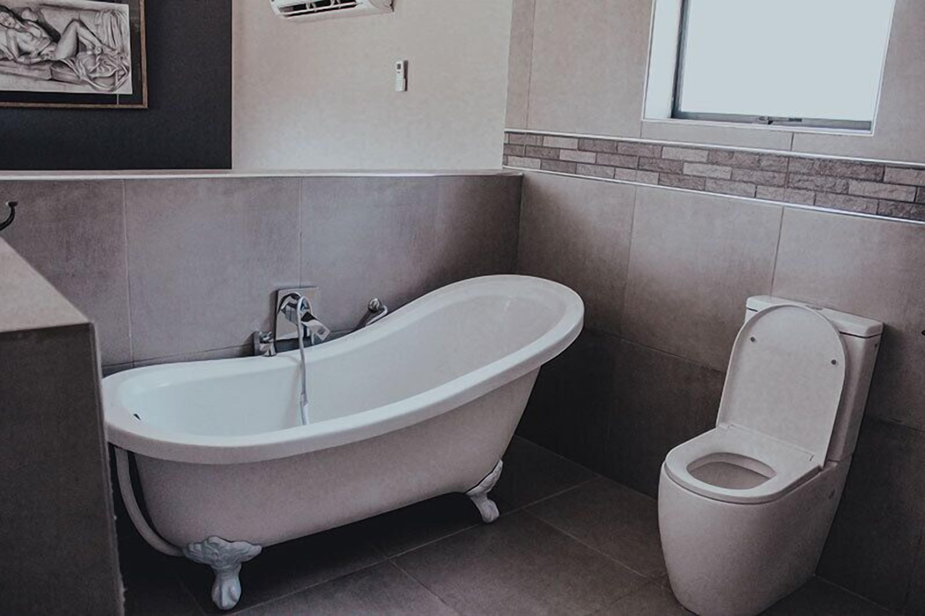 A bathroom with a freestanding bathtub, a toilet, and a framed artwork on the wall.
