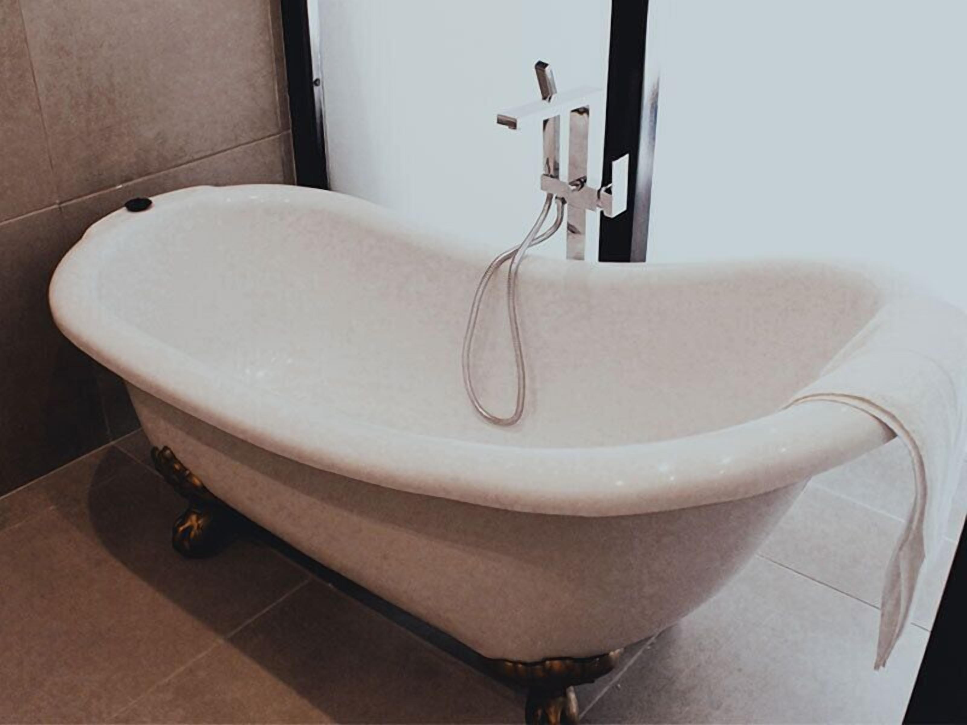 A freestanding bathtub with a modern design, positioned in a bathroom with tiled flooring and a door in the background.