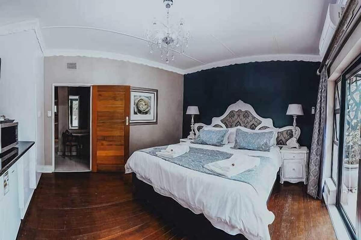 A bedroom with a large bed, bedside tables, a chandelier, and a view through a window.