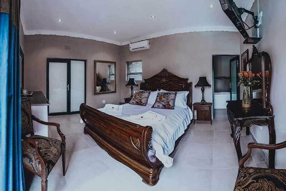 A bedroom with a large bed, a dresser, a chair, a mirror, and a window with blinds.