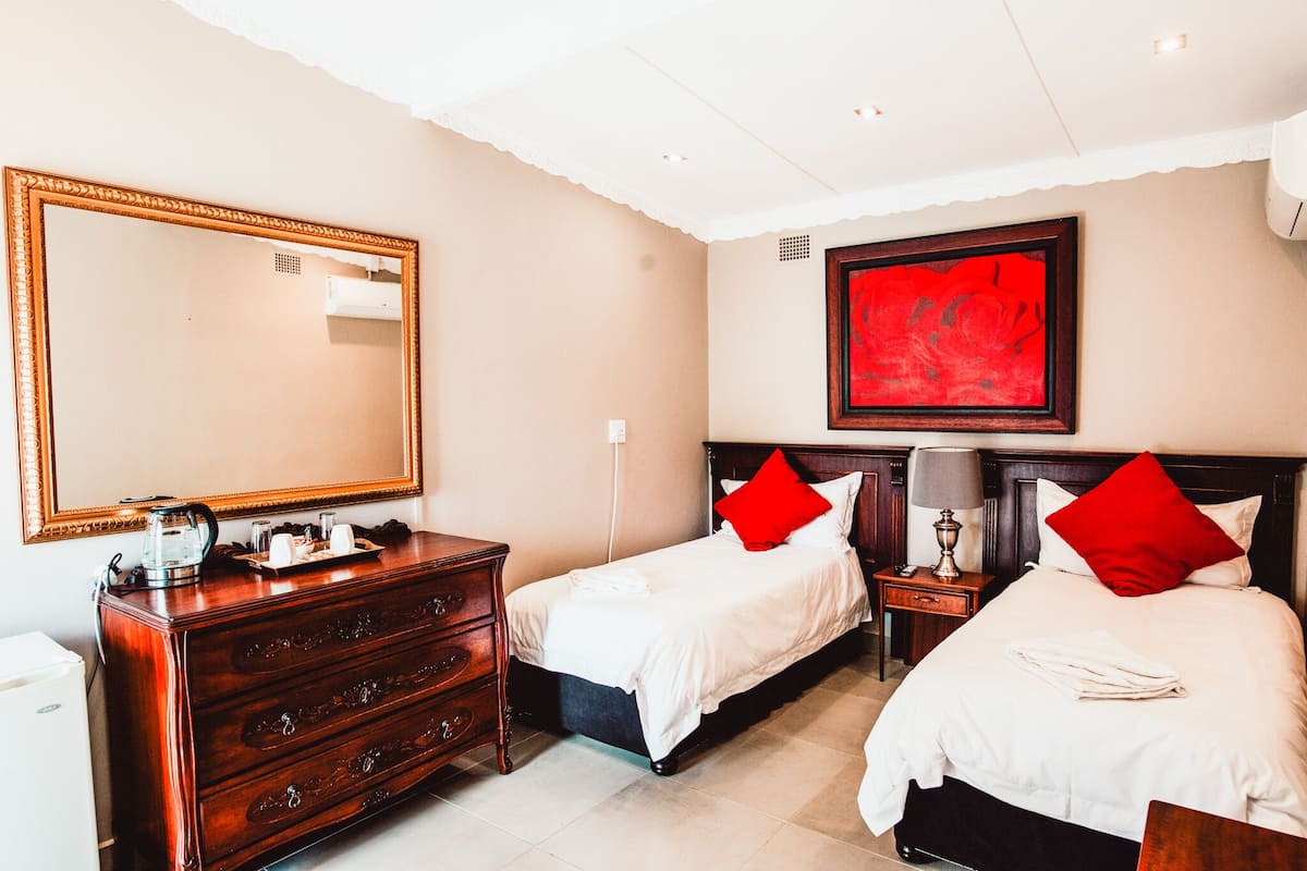A hotel room with two beds, a dresser, a mirror, a red artwork, and a nightstand with a lamp.