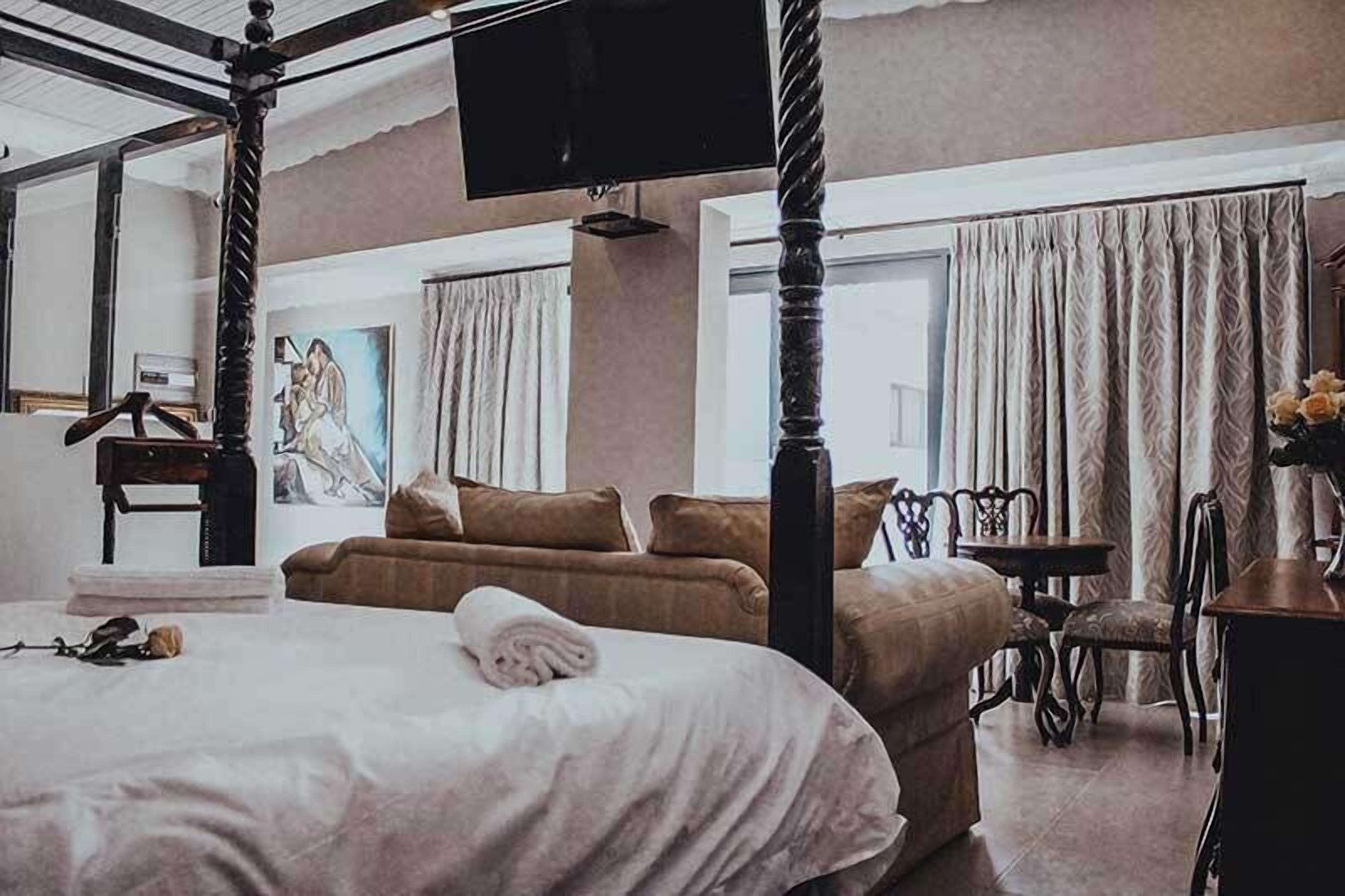 Un letto a baldacchino con una televisione sopra, un quadro al muro e una finestra con tende.