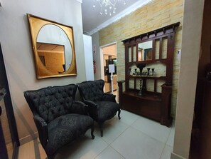 A hallway with a dark patterned sofa, a large mirror, and a wooden cabinet with a candle holder.