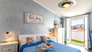 A bedroom with a bed, bedside tables, a tray with cups and pastries, a wall sign, and a view of the outdoors. - Sunset Bay Tecno Home Sardinia (Valledoria)