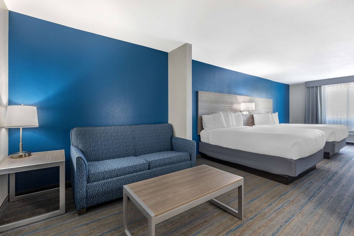 A hotel room with a blue accent wall, a sofa, a bed, a nightstand, and a coffee table.