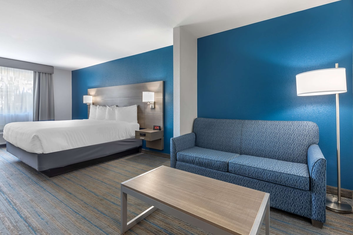 A hotel room with a bed, a sofa, a table, and a lamp.