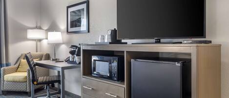 Une chambre d’hôtel équipée d’un bureau, d’une chaise, d’une télévision à écran plat, d’un four à micro-ondes, d’un réfrigérateur et d’un mini-bar.