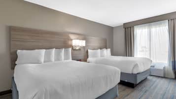 Habitación de hotel con dos camas, un ventanal con cortinas, una lámpara de pared y suelo alfombrado.
