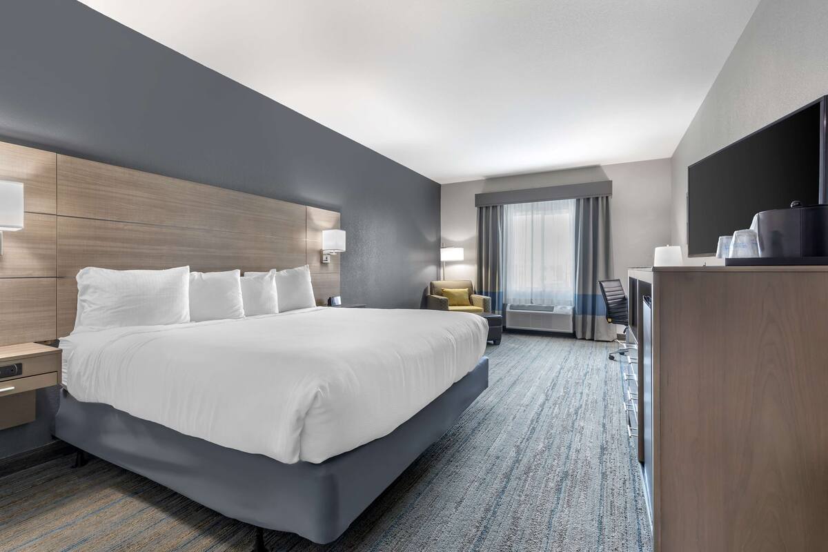 A modern hotel room with a large bed, bedside tables, a desk, and a flat-screen TV.