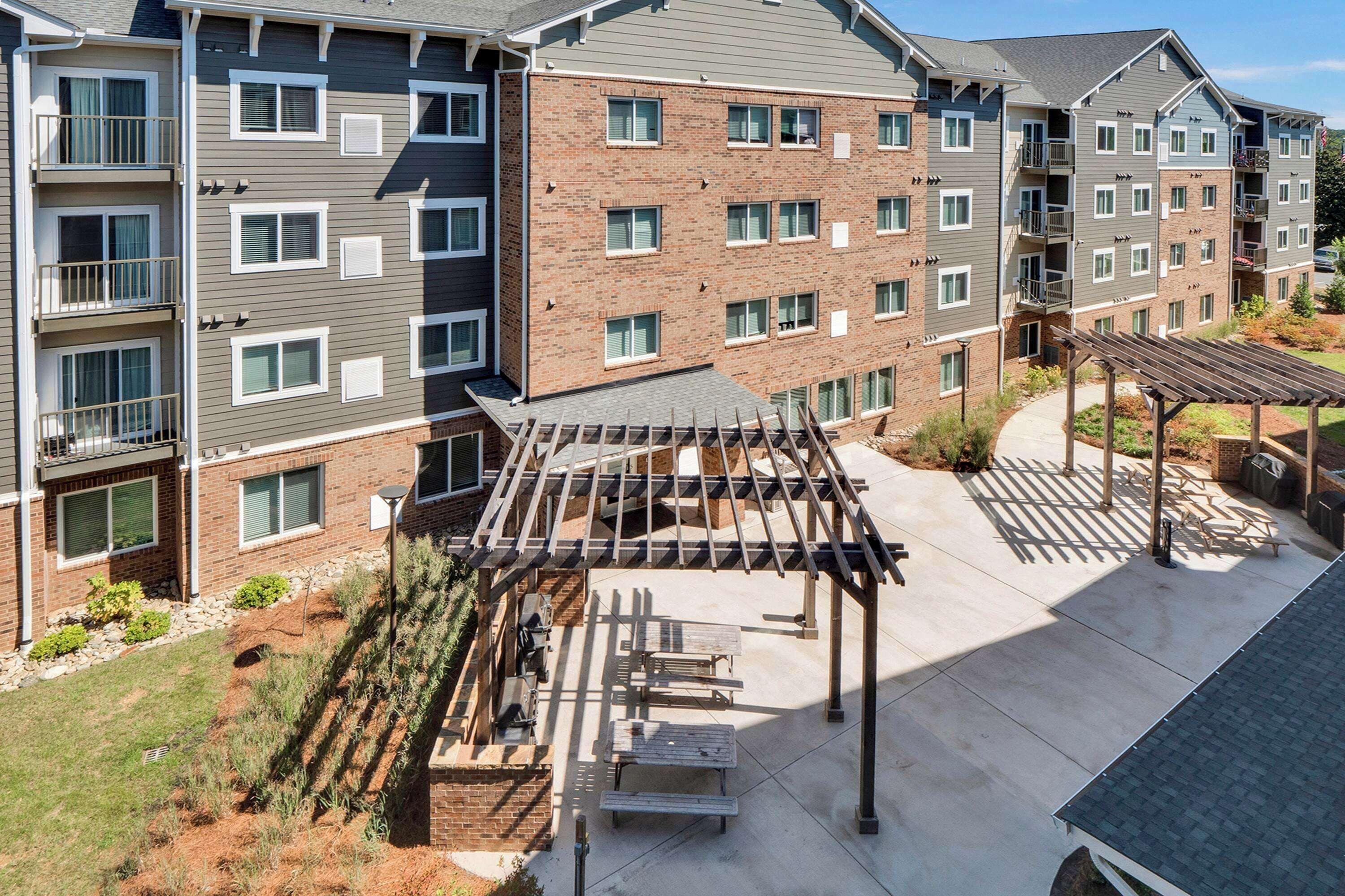 A multi-story residential building with a covered outdoor patio area, outdoor seating, and a landscaped garden.