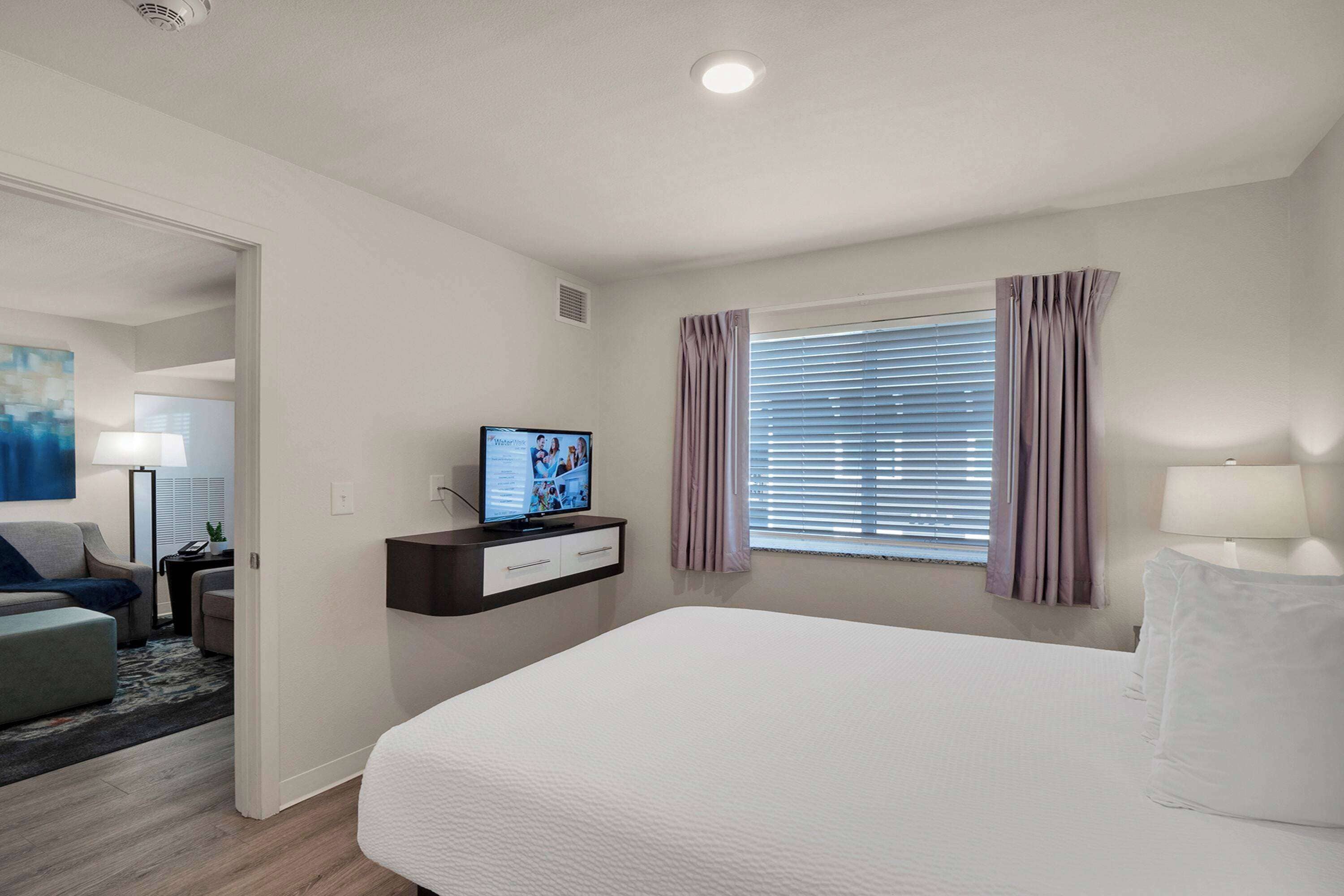 A hotel room with a bed, a television, a desk with a computer, and a window with curtains.