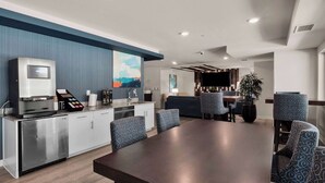 Une cuisine moderne équipée d’une machine à café intégrée, un coin repas avec une grande table et des chaises à motifs, et un espace détente avec un canapé et un téléviseur.