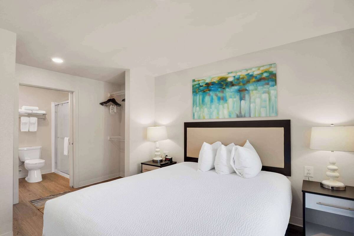 Hotelkamer met een groot bed, twee bedlampen, een hoofdbord, een schilderij aan de muur, een badkamer met toilet en douche.