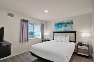 A hotel room with a large bed, two bedside tables with lamps, a TV, and a window with curtains.