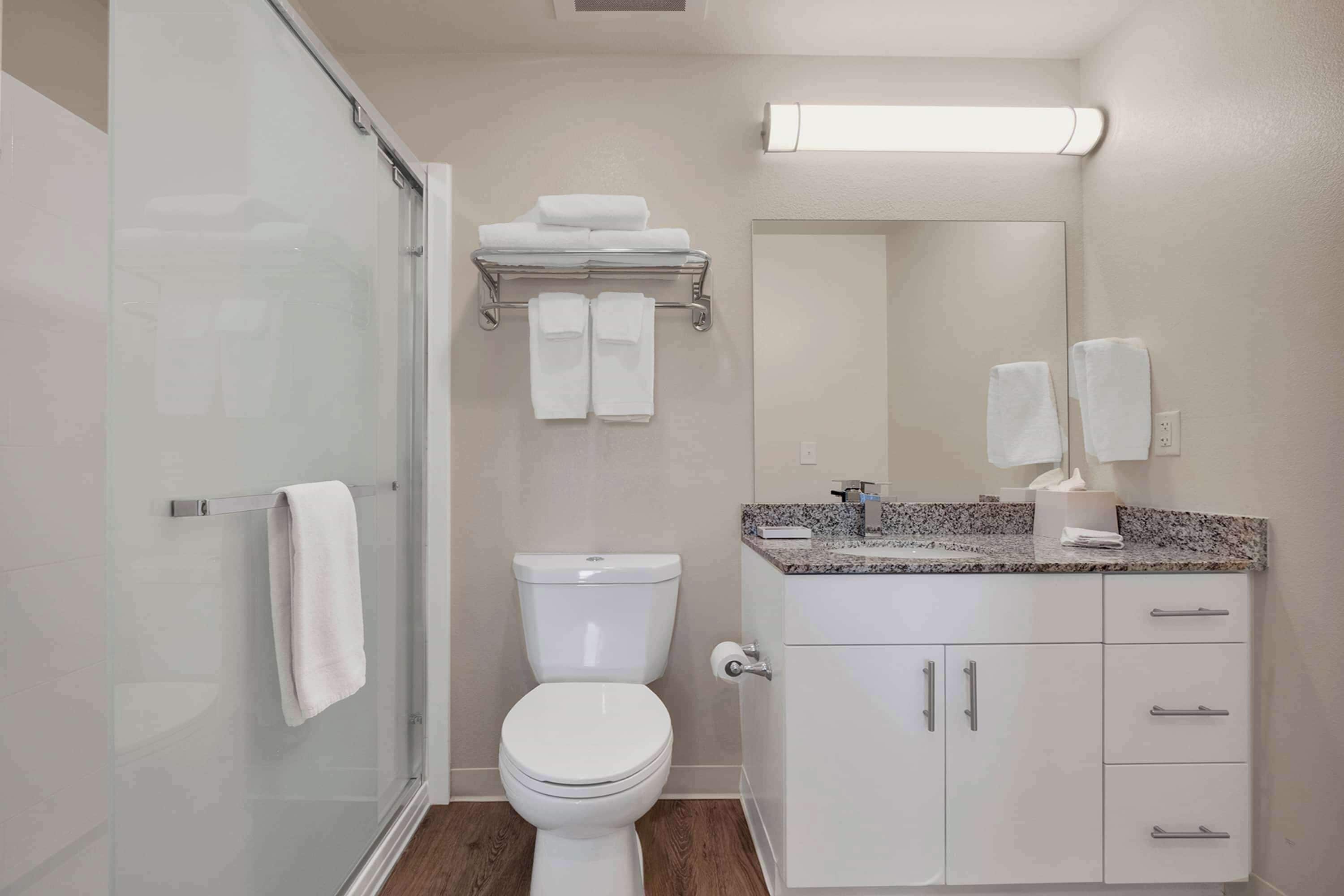 Un baño moderno con cabina de ducha de vidrio, inodoro, tocador con encimera de granito y espejo.
