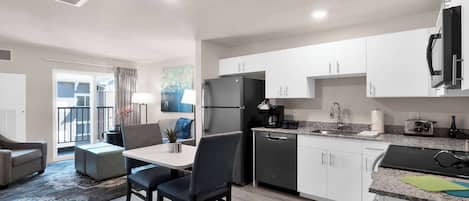 A modern kitchen with white cabinets, a stainless steel refrigerator, and a granite countertop.