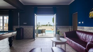 Une pièce avec une table de billard, un canapé en cuir et une vue sur l’espace piscine extérieur.