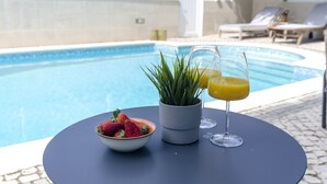 Une table au bord de la piscine, avec un saladier de fraises, une plante en pot et un verre de jus d’orange.
