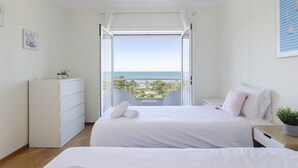 Une chambre à coucher avec un lit, une commode, une table de chevet et une vue sur l’océan.