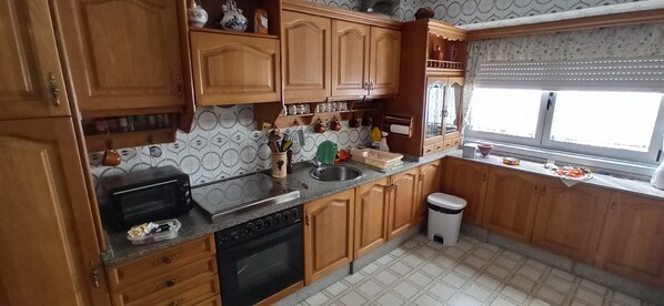 A kitchen with wooden cabinets, a stove, a sink, and a window with blinds.