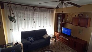A living room with a sofa, television, ceiling fan, and decorative items on shelves.