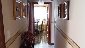 A narrow hallway with tiled flooring, framed pictures on the walls, and a wooden bench with a vase of flowers.