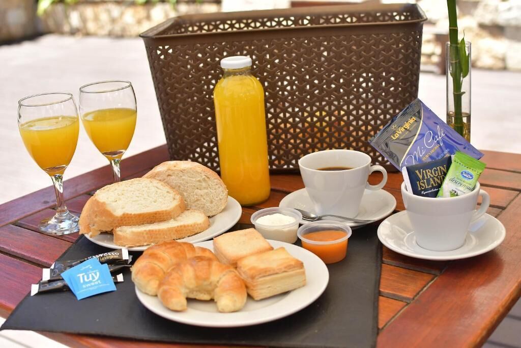 A breakfast setup with croissants, bread, juice, coffee, and a small plant.