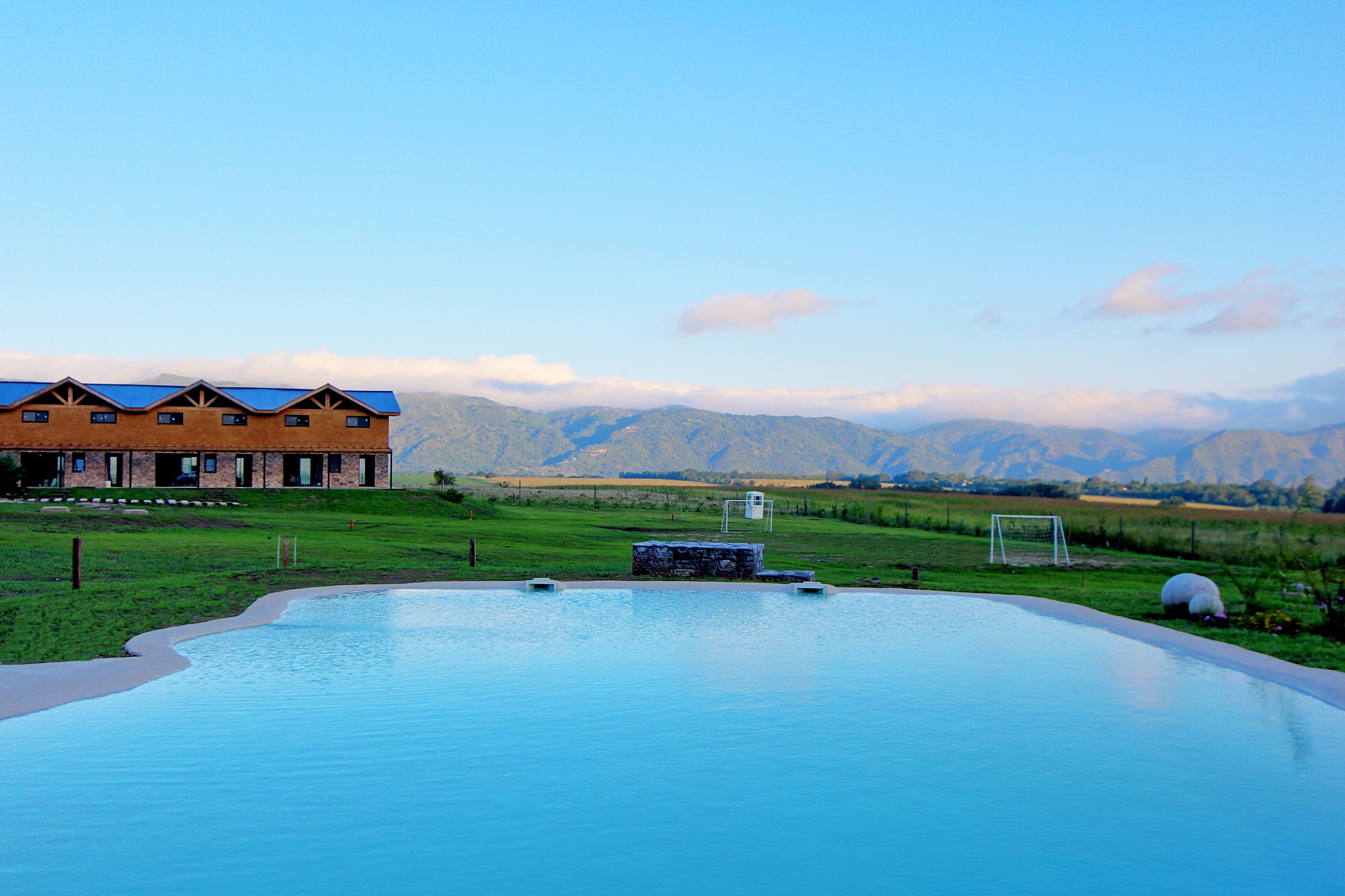 A pool with a view of mountains, a building with a blue roof, and a grassy area.