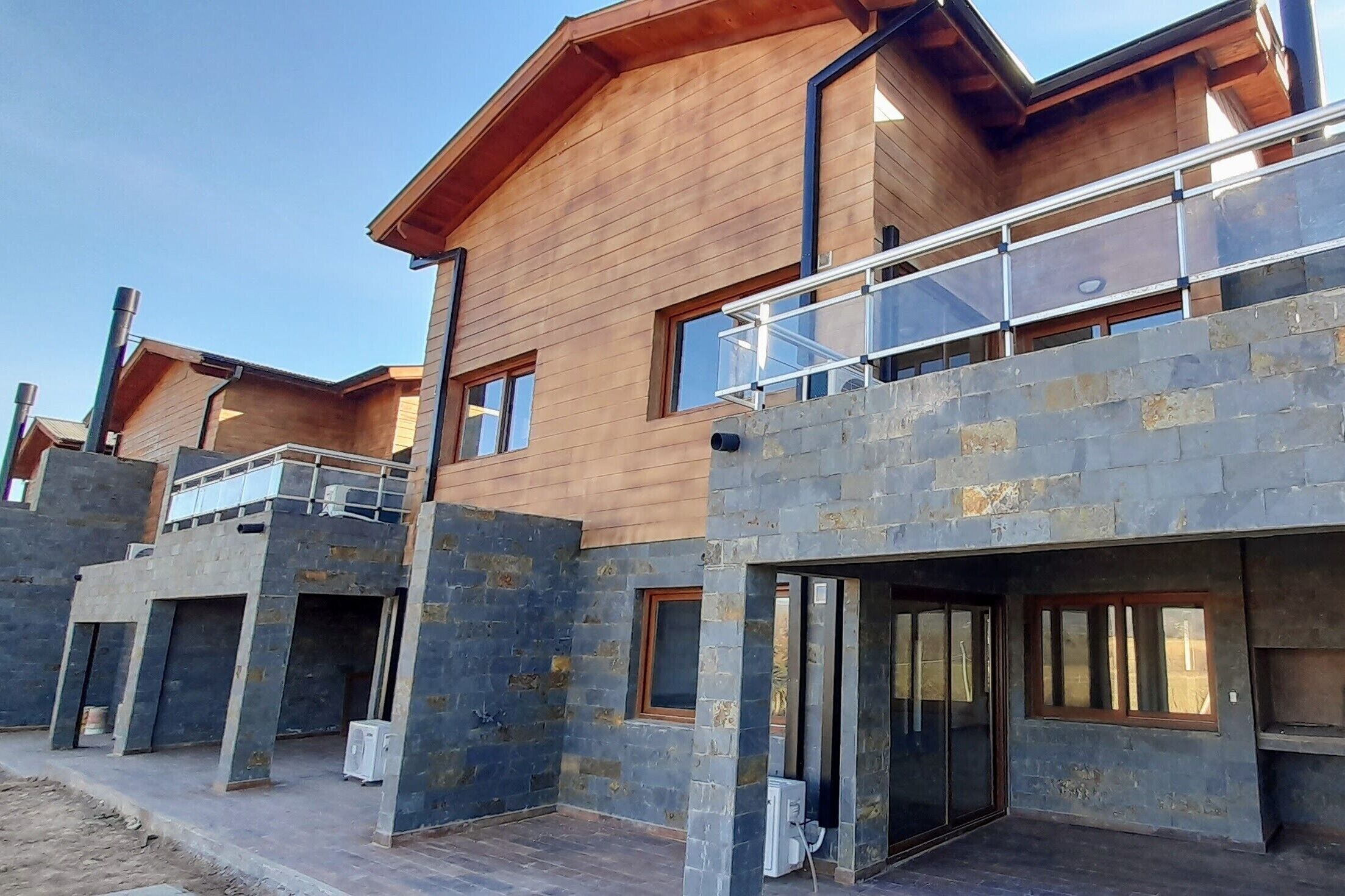 A modern building with a wooden facade and stone accents, featuring multiple balconies and large windows.