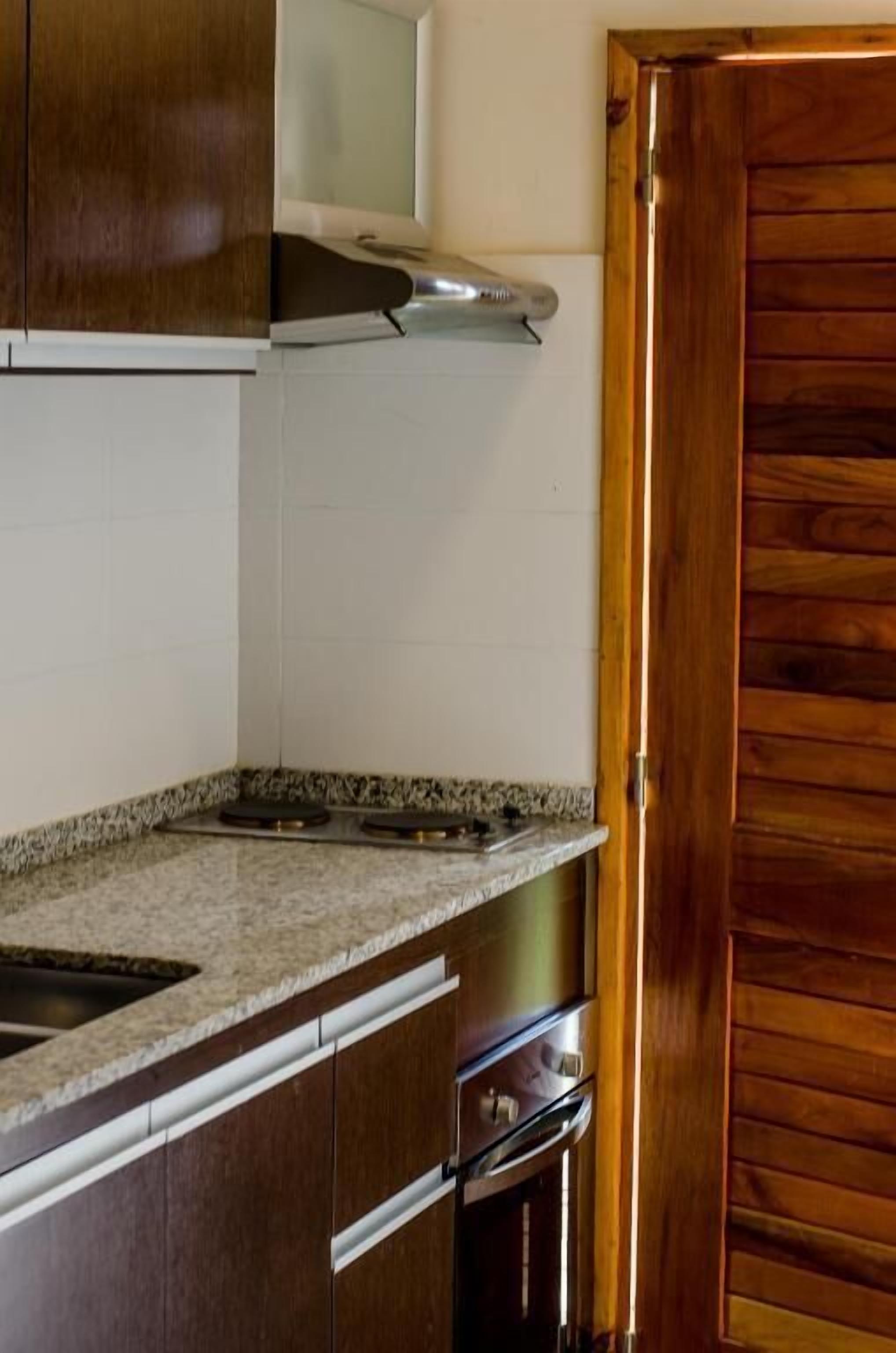 Une cuisine avec des meubles en bois, un plan de travail en granit, une hotte en acier inoxydable et une porte en bois.