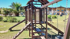 Un tobogan de fusta al parc, amb un edifici al fons.