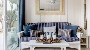 En hyggelig stue med en stribet sofa, et hvidt sofabord med stearinlys og et dekorativt spejl.