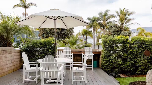 En terrasse med et rundt bord, hvide stole, en parasol og en indbygget grill.