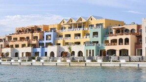 Filare di edifici alberghieri colorati con balconi, un muro in pietra in primo piano e una distesa d'acqua.