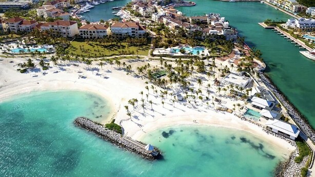 Vista aerea di un resort con diversi edifici, una spiaggia e acque cristalline color turchese.