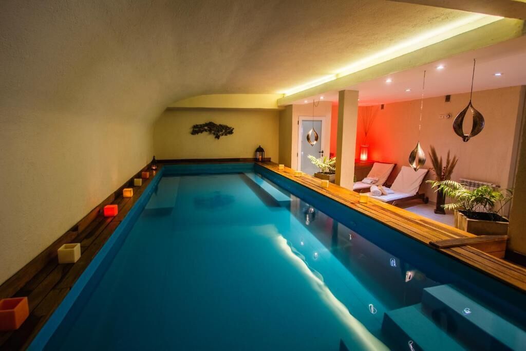 Ein großes Hallenbad mit einer Holzterrasse und einer Lounge-Bereich mit einer Couch und Pflanzen.