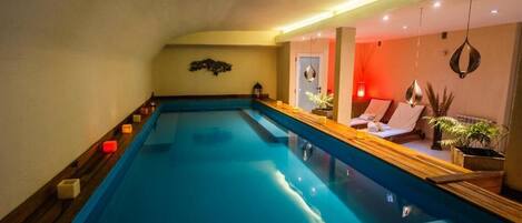A large indoor swimming pool with a wooden deck and a lounge area with a sofa and plants.