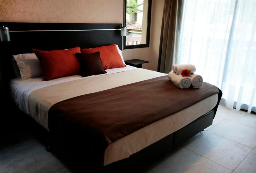 A neatly made bed with a brown bedspread, two red pillows, and a white pillow.
