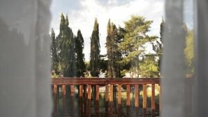 Vista a través de una ventana con barandilla de madera, árboles y cielo despejado.