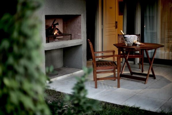 A patio with a fireplace, a table with a bottle of champagne, and a chair.