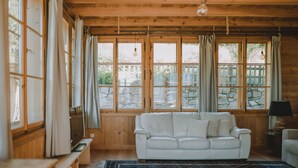 A cozy room with a white leather sofa, a patterned rug, wooden walls, and large windows with curtains. - Romantic vacation apartment on a historic estate (Platzers)