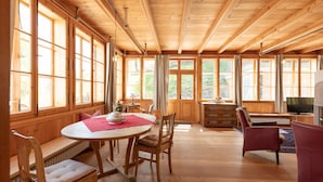 A spacious room with wooden floors and high ceilings, featuring a dining table with chairs, a sofa, and a television. - Romantic vacation apartment on a historic estate (Platzers)