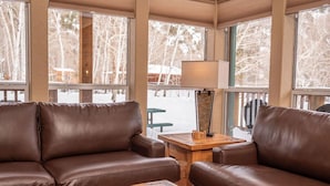 A cozy living room with leather sofas, a wooden coffee table, and a floor lamp. Large windows offer a view of a snowy outdoor deck. - Mt. Harvard Chalet at Creekside chalets (Salida)