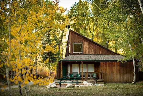 Een eenvoudige houten hut met een veranda, een groot raam en een picknicktafel.
