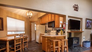 A kitchen with wooden cabinets, a central island with stools, a stove, and a television. - Mt. Harvard Chalet at Creekside chalets (Salida)