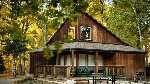 A rustic wooden cabin with a porch, picnic table, and benches. - Mt. Harvard Chalet at Creekside chalets (Salida)