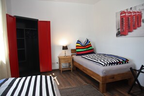 A bedroom with a bed, a nightstand, a lamp, a red wardrobe, and a wall art of red telephone booths.